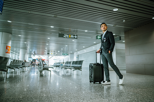 An Asian Chinese businessman walking through an airport departure area with his luggage. Business on the move.