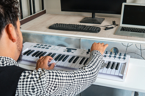 Musical producer composing a song with the keyboard and the computer.
