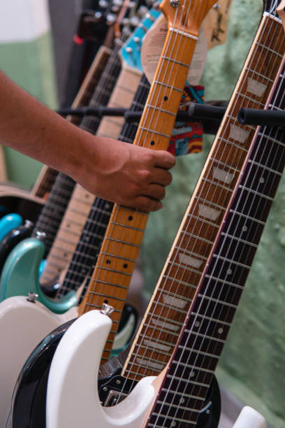Portrait of professional seller standing in music shop and showing collection of guitars for sale.