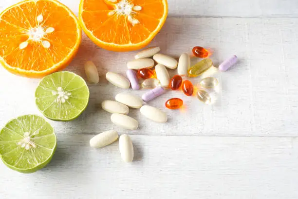Multivitamins and supplements with fresh orange and lamon on white wooden background.