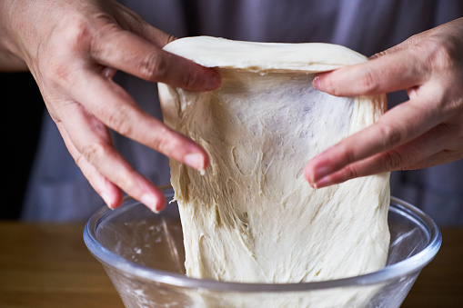 Dough in the hands of a woman cook on a wooden background with flour and wheat ears. Cooking concept.