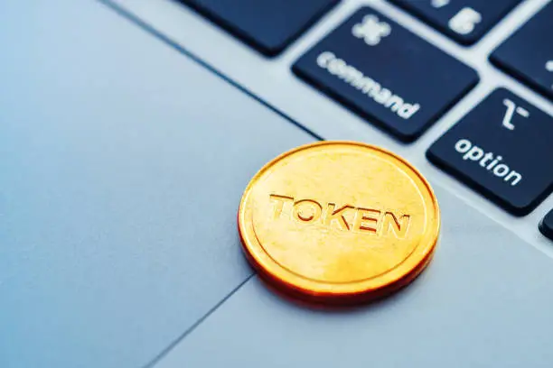 Photo of Text Token written on a golden coin lying on the modern laptop. Concept of cryptocurrency, digital technologies in business.