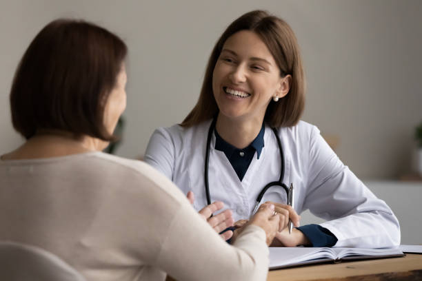 une femme médecin généraliste souriante écoute une visiteuse âgée en réunion - general practitioner photos et images de collection