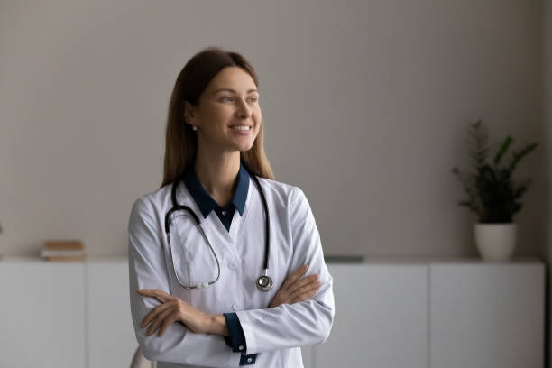 confident young woman doctor stand in office with crossed arms - médico geral imagens e fotografias de stock