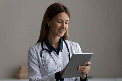 Doctor online. Smiling female doc therapist gp use tablet pc in hospital read electronic case history record answer patient question in chat. Happy modern day woman medic work at web on digital pad