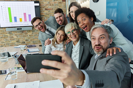 Large group of happy entrepreneurs having fun while taking a selfie with cell phone in the office.