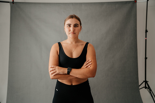 Seriously focused female standing crossed arms in a studio in her sports wear and wearing her new smart watch. High quality photo