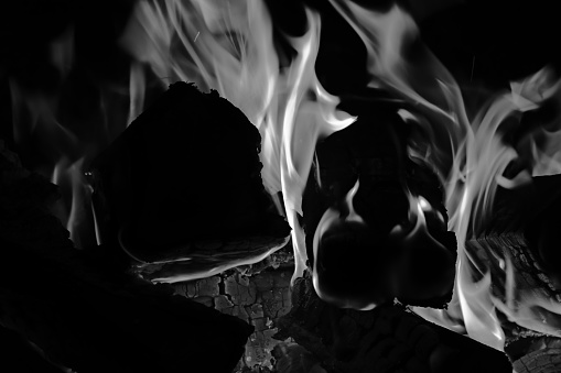 Fireplace with burning wood and forks of flame. Close-up view. Black and white toned image.