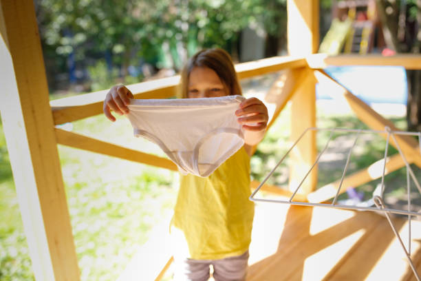 девочка в футболке вешает сухие детские трусики на сушилку на улице летом, детский энурез, помогая маме - enuresis с�токовые фото и изображения