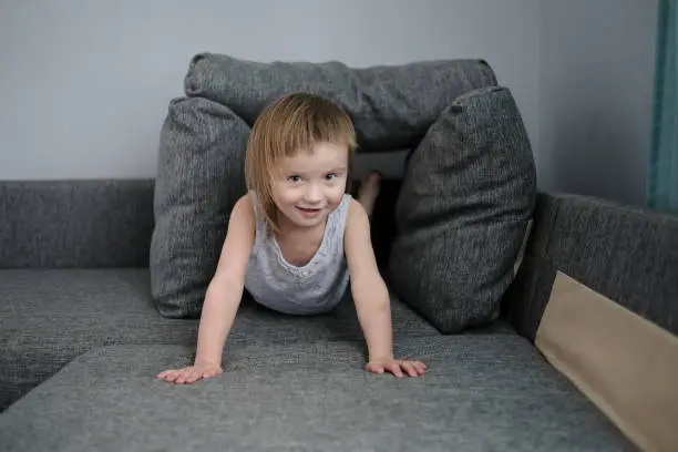 Photo of funny European child playing with pillows on couch