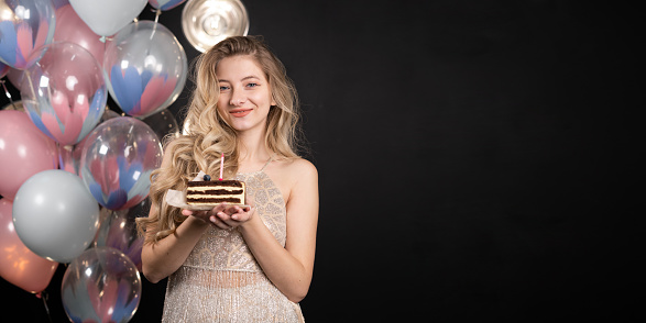Happy girl with balloons .young girl standing in a dress with a piece of birthday cake black background, laughing cheerfully emotion of joy and delight. Banner. copy space.