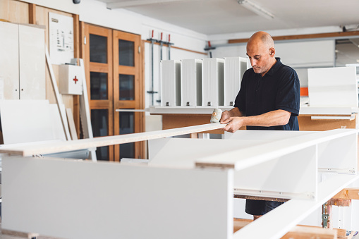 Caucasian man, carpenter assembling furniture out of white chipboard in the workshop. Man working for furniture manufacturing firm.