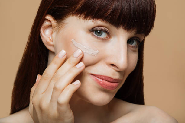 cosmética de belleza. de cerca hermosa mujer de cabello rojo aplicando base de crema tonal en la cara. - imagen virada fotografías e imágenes de stock