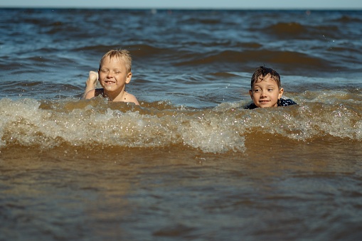 7-8 years old cute caucasian boys swim in the sea with big splashes. Children enjoys swimming in the ocean. Holidays, vacation with kids. Image with selective focus