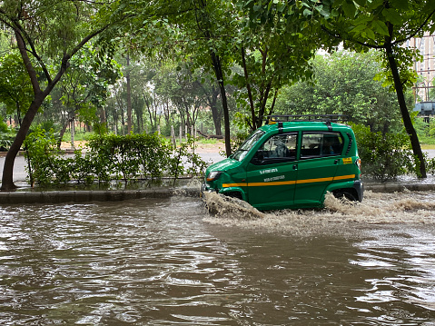 Ghaziabad, Uttar Pradesh, India - July 20, 2022: Stock photo showing traffic on a flooded road in a residential area, green and yellow auto taxicab driving through waterlogged land caused by monsoon season.