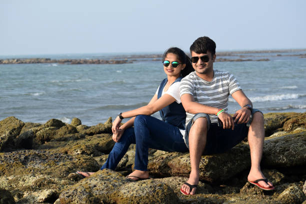 feliz pareja joven sentada en los corales del mar apoyándose cerca del mar. hombre y mujer jóvenes disfrutando de las vacaciones - honeymoon beach couple heterosexual couple fotografías e imágenes de stock