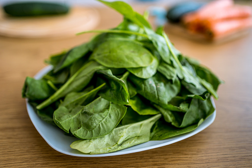 Green fresh spinach leaves on a plate on wooden table