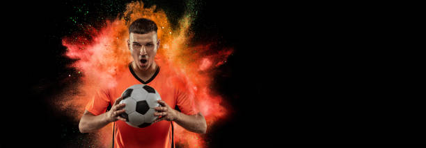 istock Creative sport collage with young man, professional soccer player setting to win isolated on black background with powder splash. Victory, energy, sport. Bright emotions 1410246566