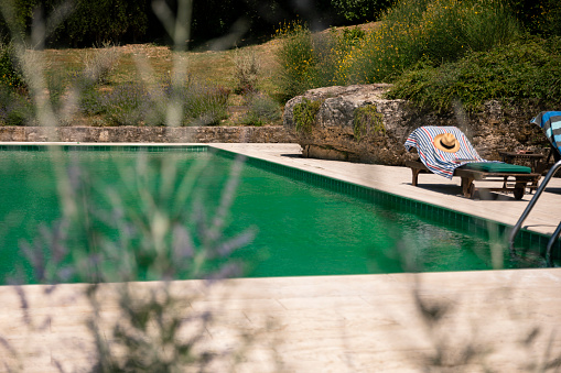 A swimming pool at vacation rental in Tuscany, Italy. There is a sun lounger with a swimming towel and sun hat on it.