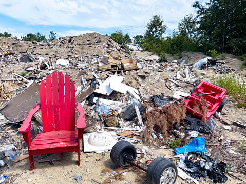 A vivid red wooden lounge chair is surrounded by trash at a dump.