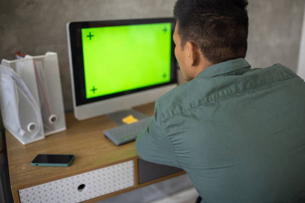 Rear-view of unrecognizable man Japanese ethnicity working on computer. \nChroma key on computer display