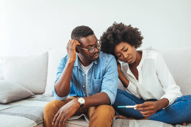 A sad young woman holds a pregnancy test in her hand. A sad young woman holds a pregnancy test in her hand. The concept of unwanted pregnancy. Sad stressed couple with pregnancy test sitting at home. Worried about the serious consequences infertility stock pictures, royalty-free photos & images