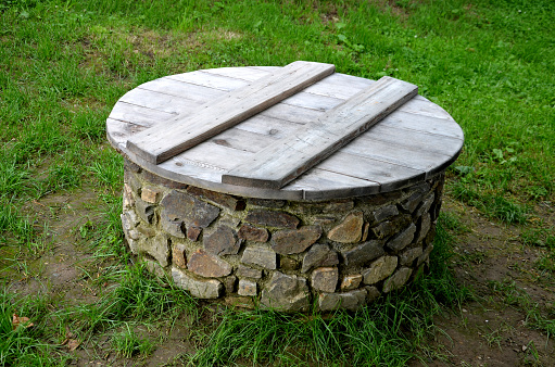 stone round fountain with a protective grid of twisted prisms. forged steel bars go spiraled at the top. around the well there is a retaining wall and a lawn. protection against falling into the depth, hatch