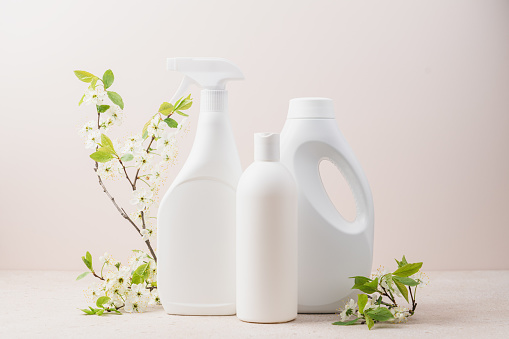 Set of white bottles with cleaning products and blossoming tree branches on beige background