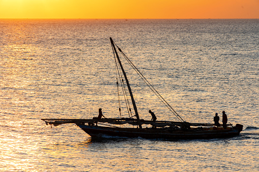 yelow sunlight on the horizon with a fishing dhow heading out to sea at night or early morning