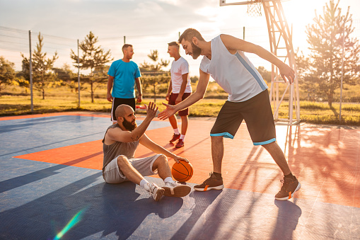 Young man picking up his friend off the ground. Group of friends playing a basketball game outdoors.
