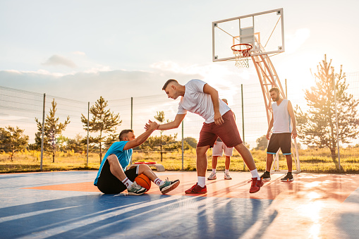 Young man picking up his friend off the ground. Group of friends playing a basketball game outdoors.