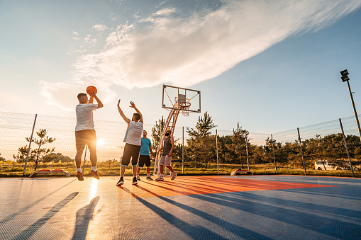 Group of friends playing basketball on a basketball court outdoors.