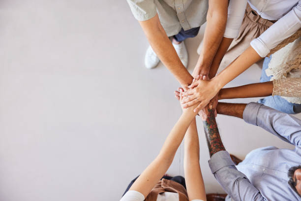 Diverse businesspeople standing together with their hands stacked High angle view of a diverse group of unrecognizable businesspeople standing in a huddle with their hands together hands clasped stock pictures, royalty-free photos & images