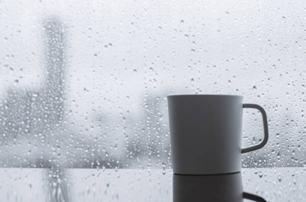 A cup of coffee puts on table in morning with rain drop on window. Stay home and relaxing concept.