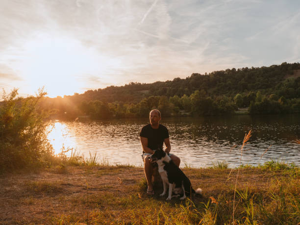 istock Man and his dog outdoors by a river at sunset in summer 1410262394