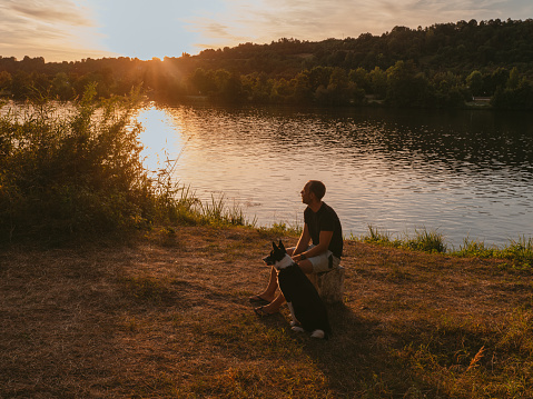 Man and his dog outdoors by a river at sunset in summer\nBeautiful sunset in DOnau Danobe river