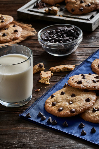Homemade chocolate chips cookies with glass of milk on a rustic wooden table
