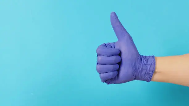 The hand is wearing a violet or purple latex glove and do like handsign on blue background.