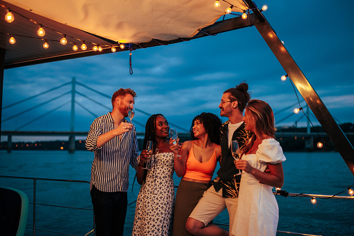 Five multiracial friends enjoying at boat party, and drinking champagne