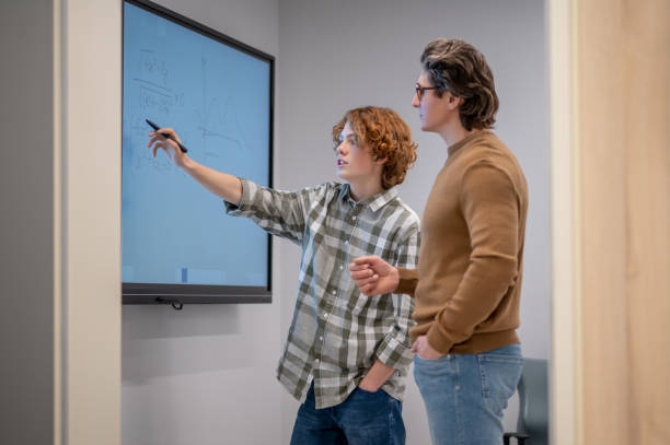 istock Ginger boy writing on the board, teacher standing next to him 1410273166
