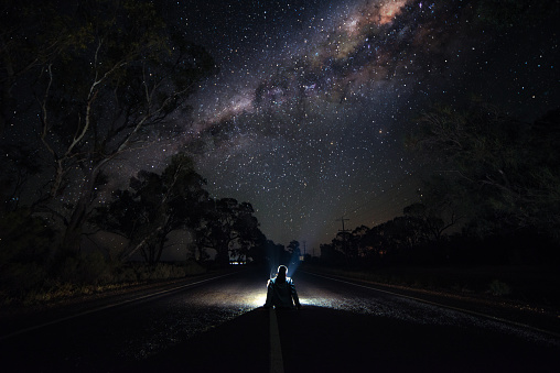 Young Man Sitting on Highway at Night Watching the Milkyway. Traveler and Astro Photography Concept