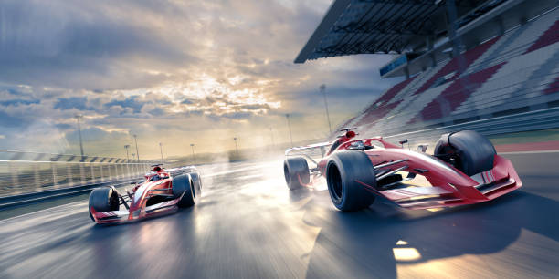 Two Race Cars Moving at High Speed in Slightly Wet Conditions Two generic red and silver racing cars moving a high speed with motion blur. The race cars are racing past an empty grandstand in slightly wet conditions, emitting sprays from wheels, under a bright and cloudy sky.  Location is fictional. motor racing track photos stock pictures, royalty-free photos & images