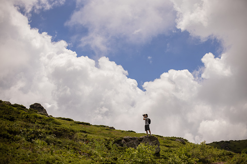Unrecognizable man on the mountain, taking photos with camera while hiking