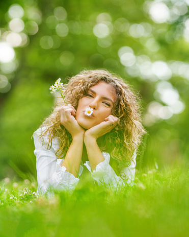 Smiling girl portrait with a flower in the mouth enjoys summer in the field.