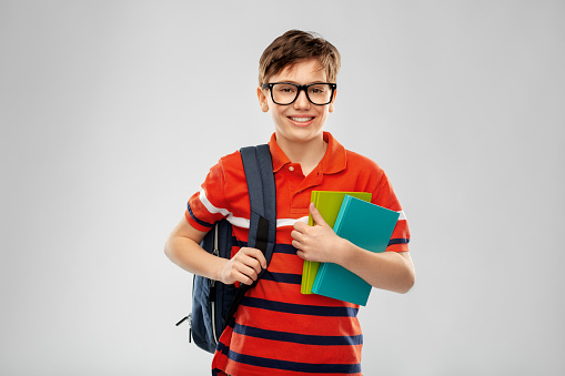 school, education and people concept - smiling student boy in glasses with backpack and books over grey background