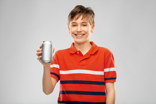 drinks and people concept - happy smiling boy in red polo t-shirt holding soda drink in tin can over grey background