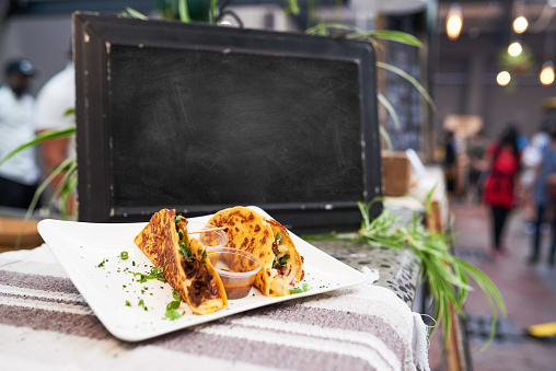 An empty chalkboard at a market with soft shell tacos in foreground. High quality photo