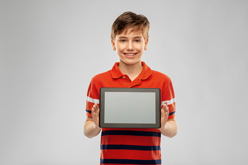 technology, communication and people concept - happy smiling boy in red polo t-shirt showing tablet pc computer over grey background