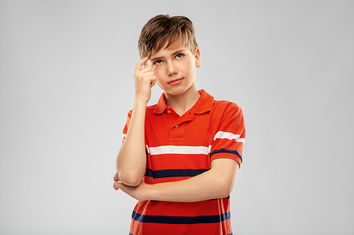 childhood, fashion and people concept - portrait of thinking boy in red polo t-shirt over grey background
