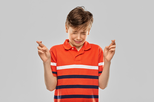 childhood, fashion and people concept - portrait of smiling boy in red polo t-shirt holding fingers crossed over grey background